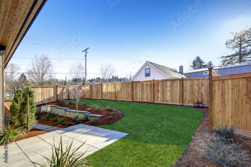 Sloped backyard surrounded by wooden fence Luxury New construction home with ope Fototapeta