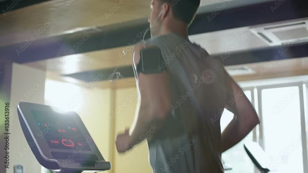 Concentrated youn man in sportswear and earphones running on treadmill at gym