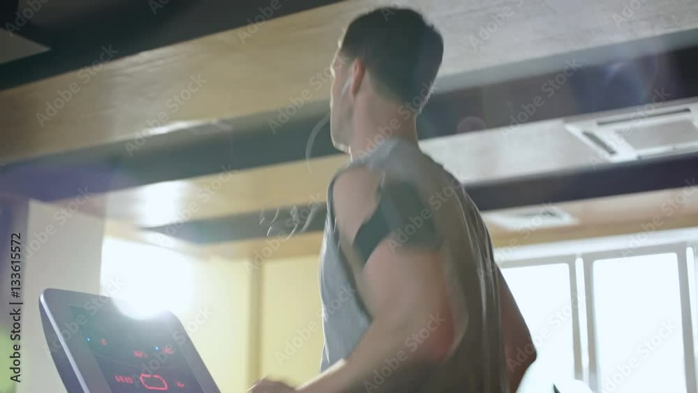 Side view of a young concentrated man in sportswear running on treadmill at gym