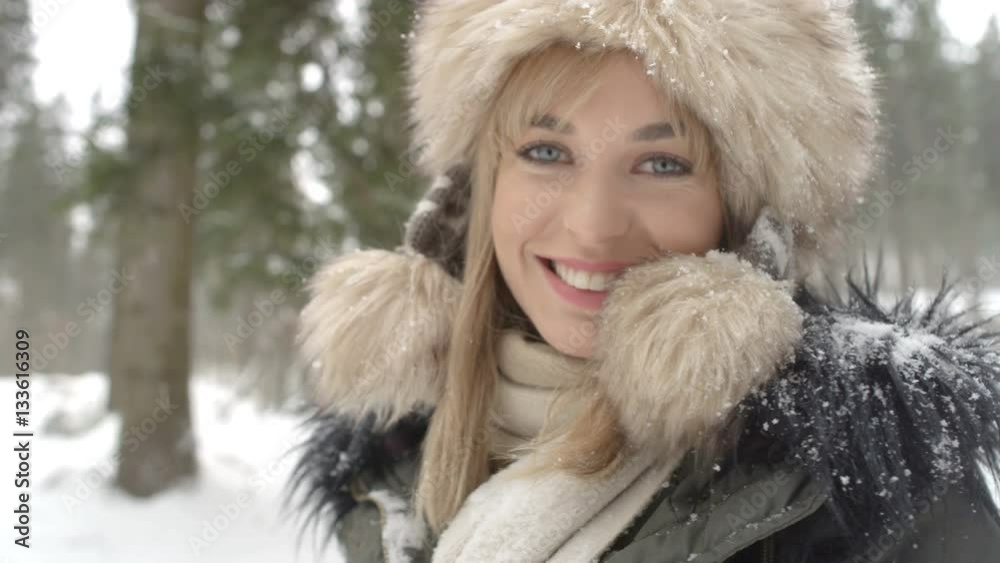 Portrait of smiling woman enjoying wintertime. Woman wearing warm clothes in a cold winter snow forest. Trees on background. Shot on Red Epic. Portrait of smiling woman enjoying wintertime. Woman wearing warm clothes in a cold winter snow forest. Trees on background. Shot on Red Epic.