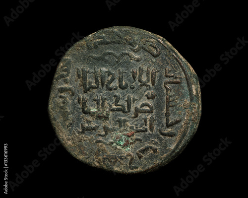 Ancient islamic copper coin with text on it isolated on black