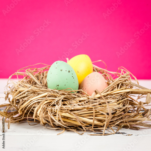 tre pastellfärgade ägg i fågelbo på rosa bakgrund