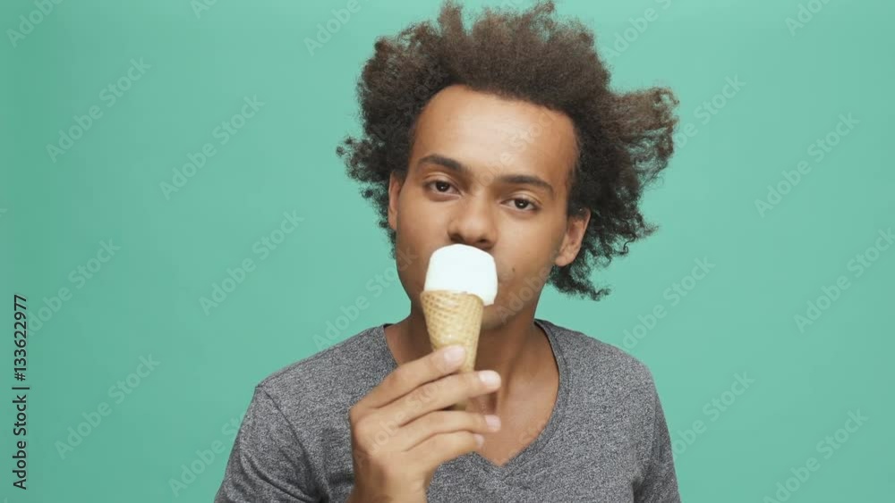 Happy afro american man eating ice cream and looking at camera isolated on the green background