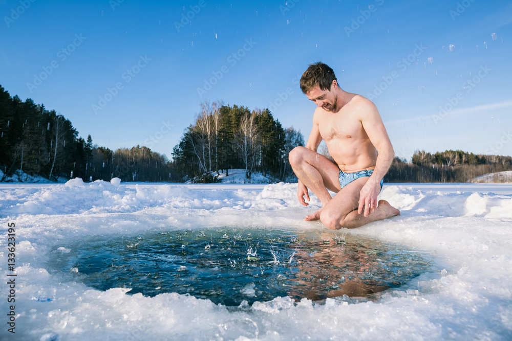 Fototapeta premium Young man going to swim in the winter lake in the ice hole