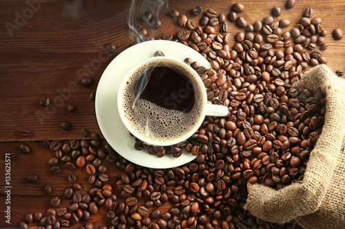 Cup of coffee with beans on table, top view