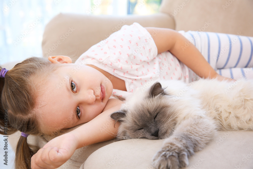 Cute little girl lying on sofa with fluffy cat