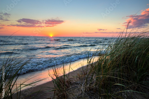 Fototapeta Naklejka Na Ścianę i Meble -  Tranquil Sunset Beach Background.  Beautiful sunset horizon over water with a sandy beach and dune grass in the foreground. Hoffmaster State Park. Muskegon, Michigan