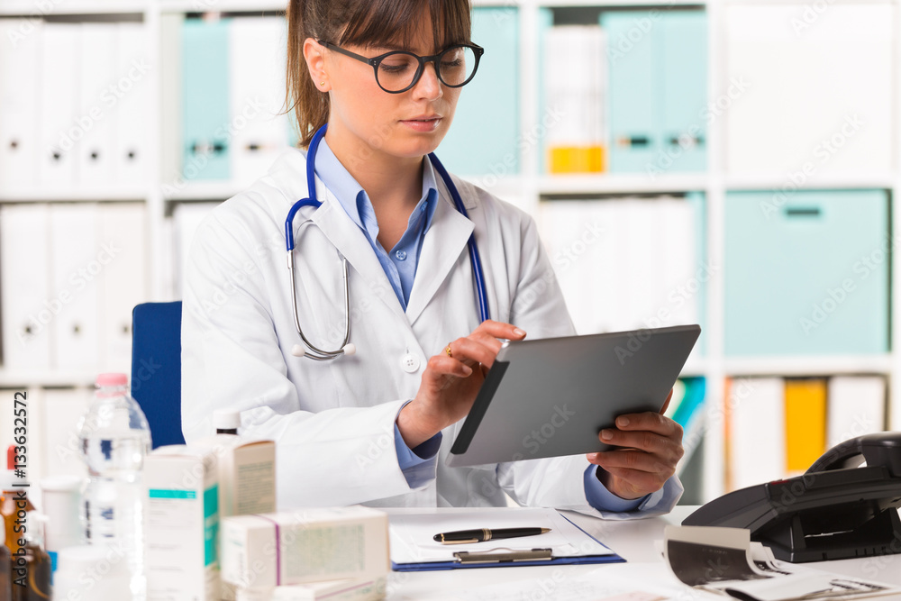 Thoughtful female doctor at desk using tablet Thoughtful female doctor at desk using tablet