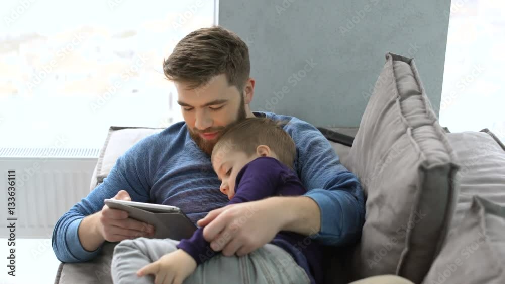 Young father and his little son having fun by gaming on a tablet while laying on a sofa at home Young father and his little son having fun by gaming on a tablet while laying on a sofa at home