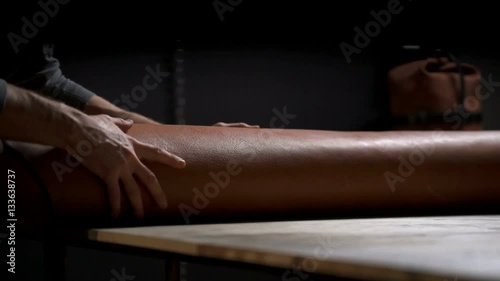A craftsman rolling out a big piece of leather on the table slow motion