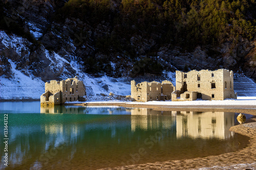 Snowy alpine lake with ruins of old houses partially submerged by water photo