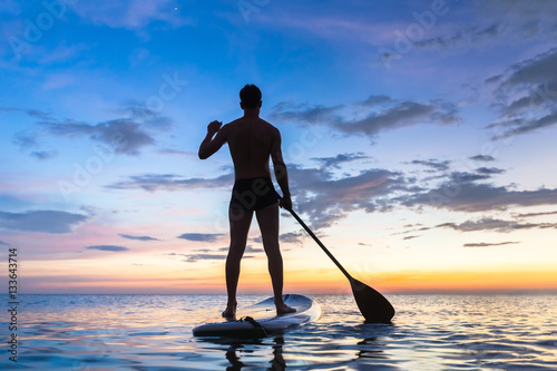Silhouette of stand up paddle boarder paddling at sunset, sea photo