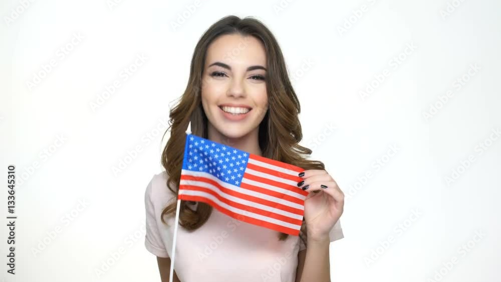 Smiling casual woman holding USA flag and pointing finger at camera isolated on a white background Smiling casual woman holding USA flag and pointing finger at camera isolated on a white background