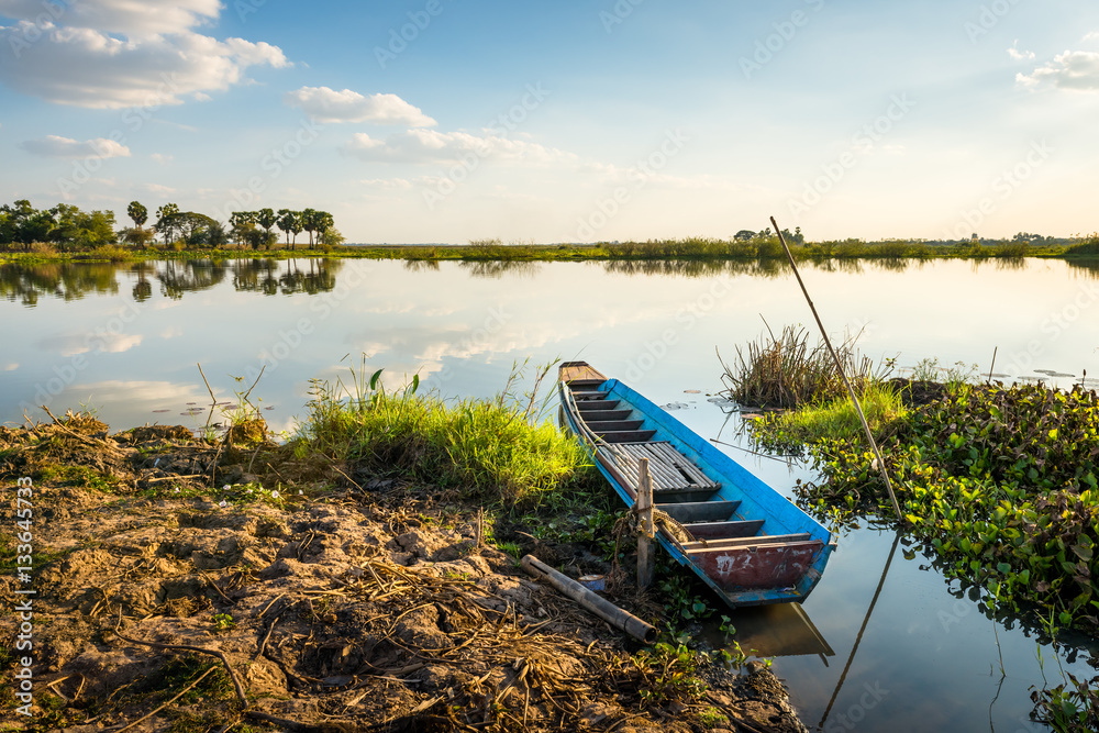 Obraz premium wooden rowboat in the calm water of lake at beautiful sunset
