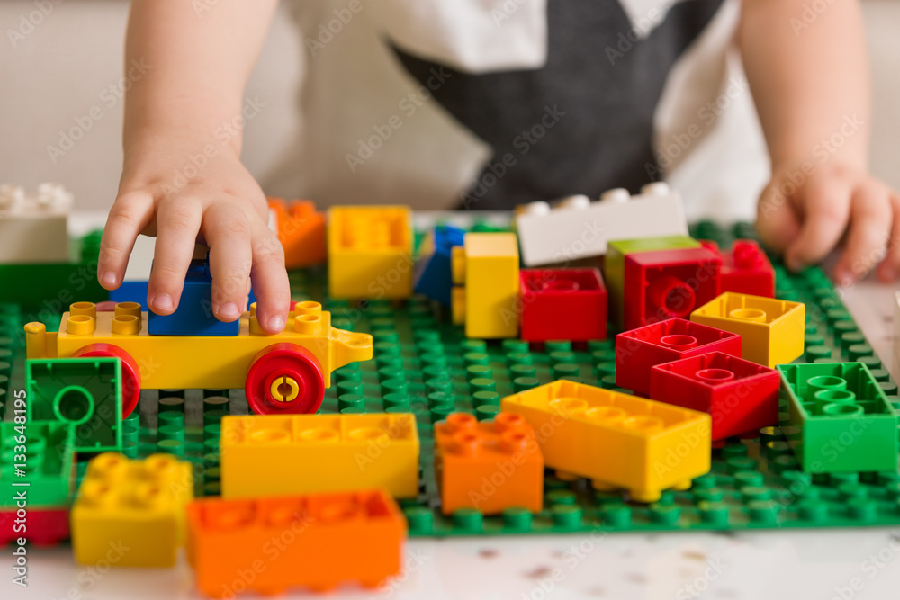 Close up of child's hands playing with colorful plastic bricks at the table. Toddler having fun and building out of bright constructor bricks. Early learning. stripe background. Developing toys Close up of child's hands playing with colorful plastic bricks at the table. Toddler having fun and building out of bright constructor bricks. Early learning. stripe background. Developing toys