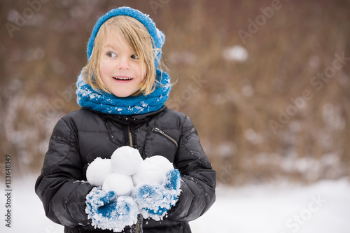 Obraz na płótnie Portrait of adorable little kid boy with long blond hair playing with snowballs outdoors