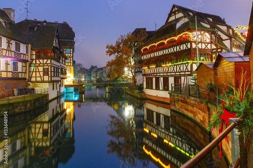 Traditional Alsatian half-timbered houses with mirror reflections in Petite France during twilight blue hour decorated and illuminated at christmas time, Strasbourg, Alsace, France