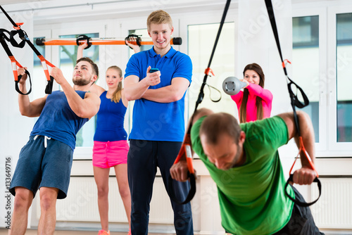 Sportler und Sportlerinnen beim Ringeturnen im Fitness-Club mit Physiotherapeut
