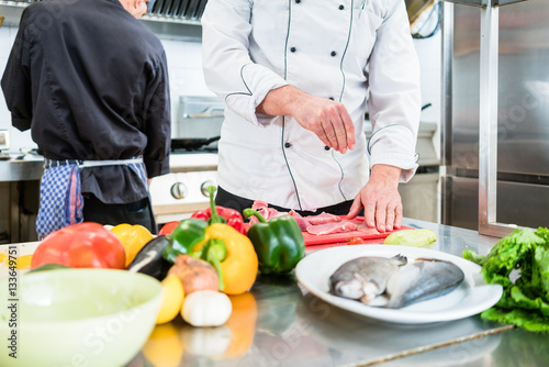 Canvas Print Chef putting salt on fish while cooking in kitchen