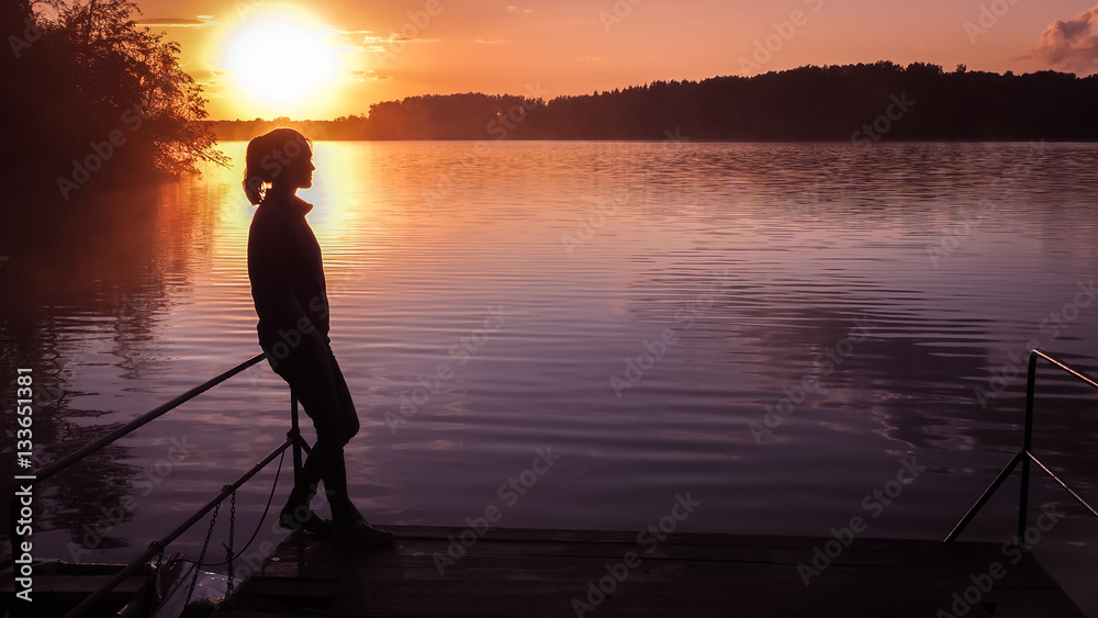 Silhouette girl background sun. Girl standing near water outdoors. Gold sunset lake. Young woman thinking about something river during golden sunset