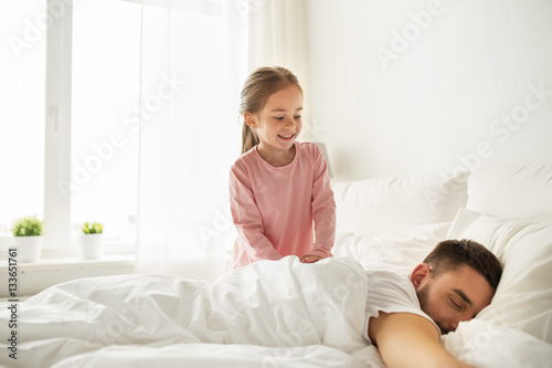 little girl waking her sleeping father up in bed