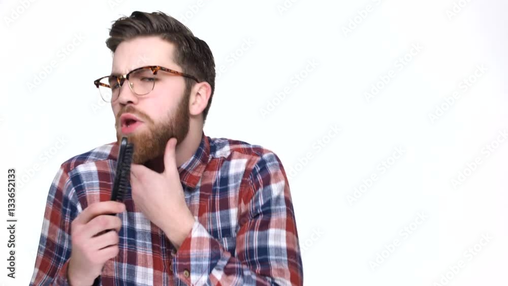 Funny young man in plaid shirt singing into comb and brushing his beard Funny young man in plaid shirt singing into comb and brushing his beard