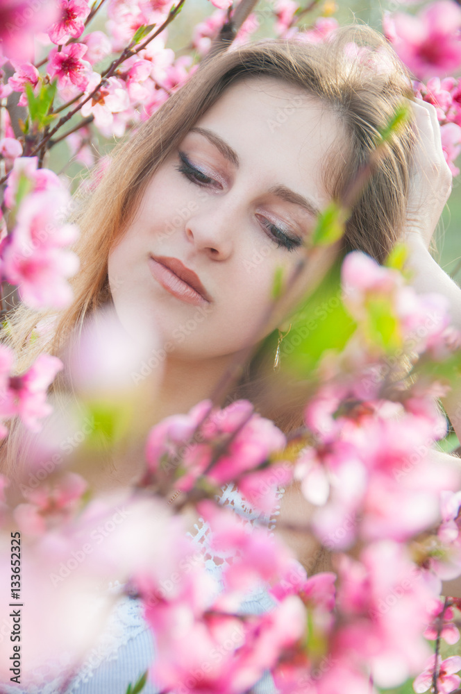 Portrait of young woman in the flowered garden in the springtime. Tender and beautiful posing.