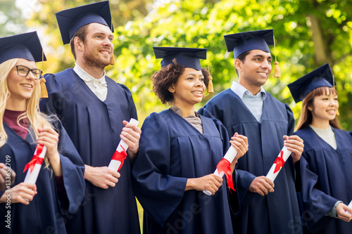 happy students in mortar boards with diplomas