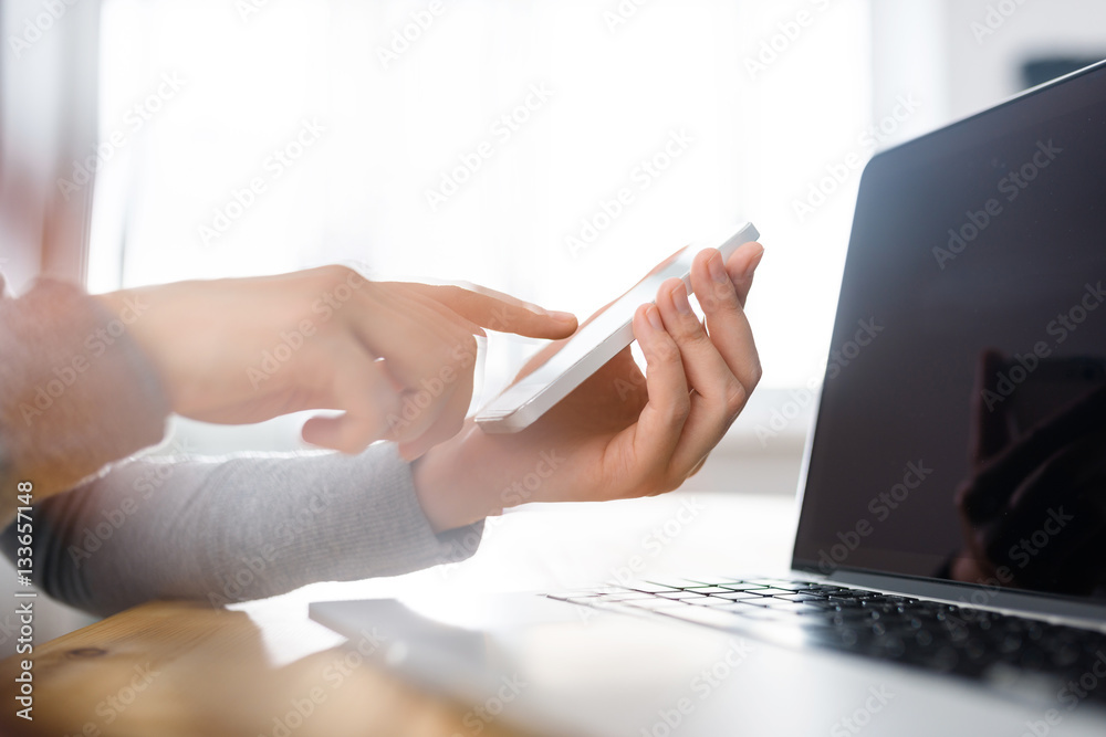 Hands typing on the phone screen online in front of open laptop, pointing, simple close up Hands typing on the phone screen online in front of open laptop, pointing, simple close up