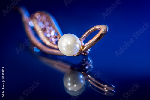 Women's Jewelry. Beautiful gold brooch with pearl - reflection on blue background