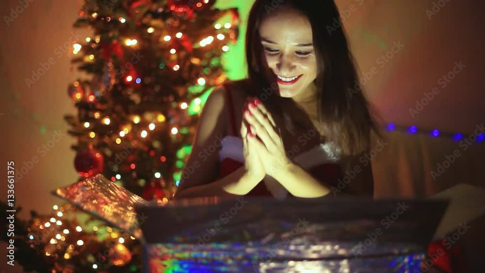 Young happy woman sits next to Xmas tree at decorated home with magical Christmas present. 1920x1080 Young happy woman sits next to Xmas tree at decorated home with magical Christmas present. 1920x1080