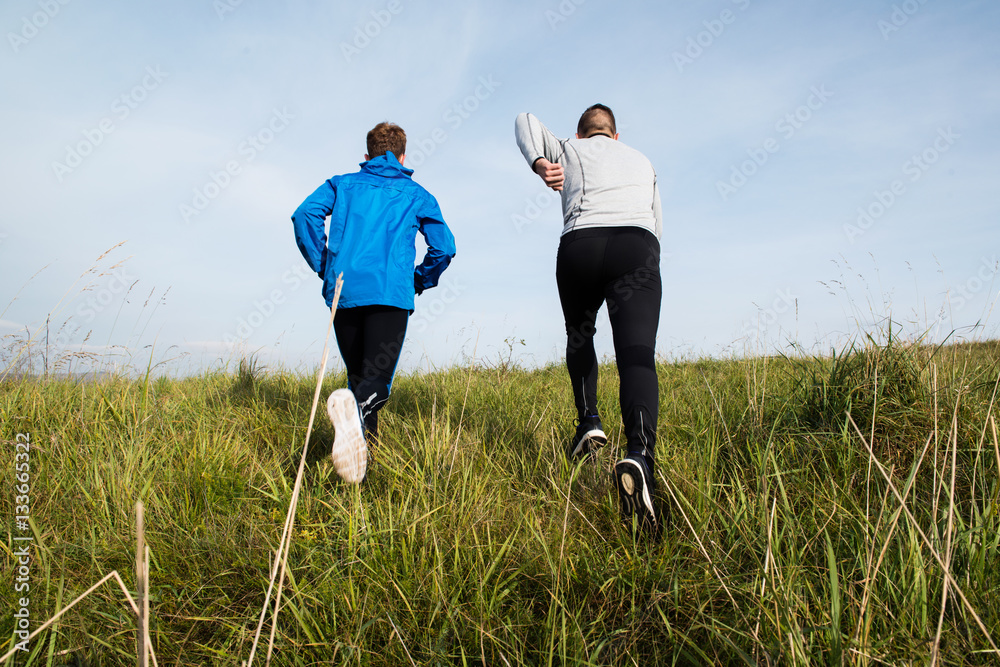 Two young athletes running in sunny autumn nature, rear view. Two young athletes running in sunny autumn nature, rear view.