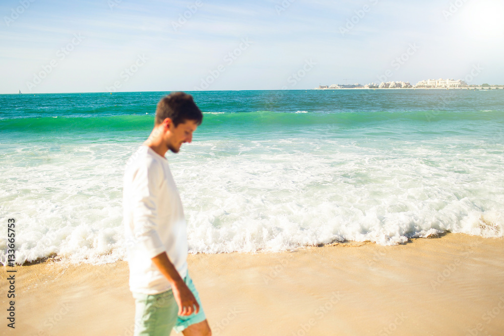 Thoughtful young man in white hoodie walks along the beach befor Thoughtful young man in white hoodie walks along the beach befor
