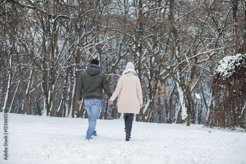 Happy loving couple walking in winter park enjoying snow