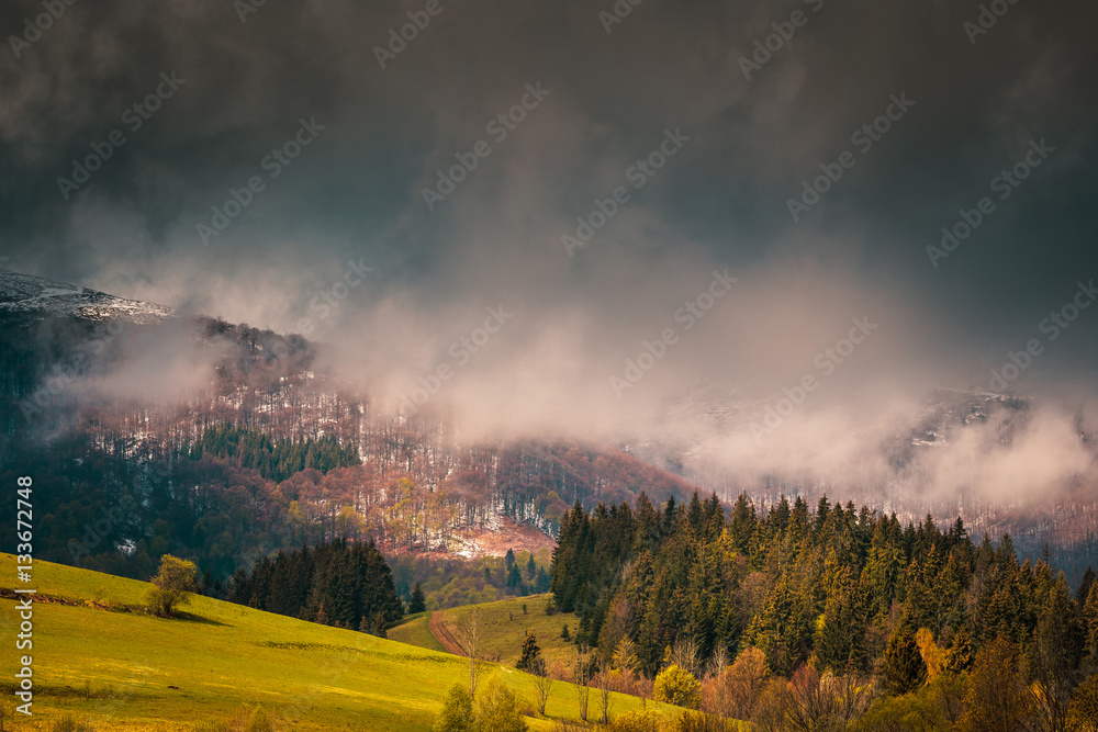 Beautiful dramatic clouds over mountains. Sunlight spots on the forest hills at Carpathian mountains. Ukraine.