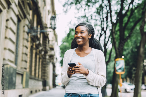 Foto Knee figure of young beautiful black woman walking outdoor in the city using sma