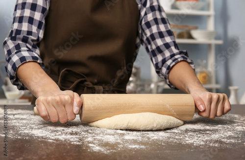 Young woman rolling out dough in kitchen