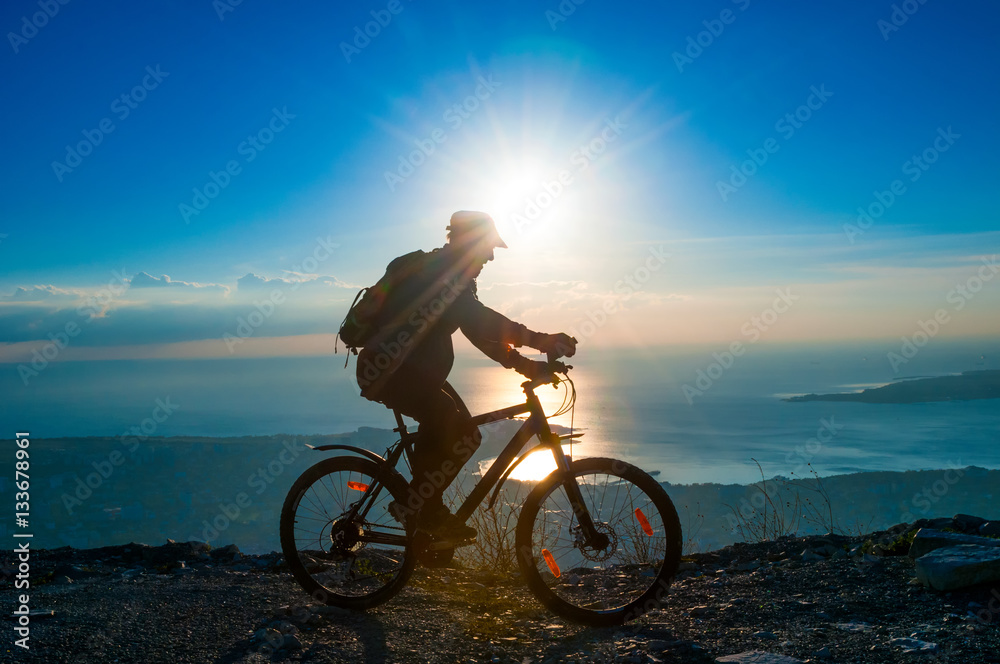 Obraz premium Silhouette of senior cyclist rides on a bike in mountain at suns