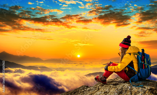 Young woman sitting on the hill of high mountains at sunrise.