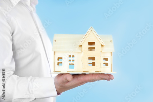 Man holding house model on light blue background