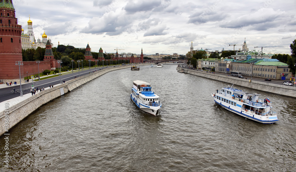 Tour boats / ships are on Moskva river. Dramatic cloudy sky is in the view. Dormition Cathedral, Kremlin Palace and Borovitskaya Tower are on the left side of the image.