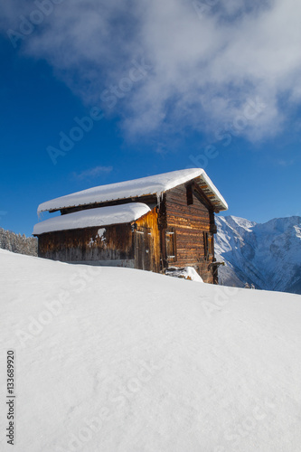 winter landscape with an old wooden cottage in front of a mountain range   © olivercesarritz
