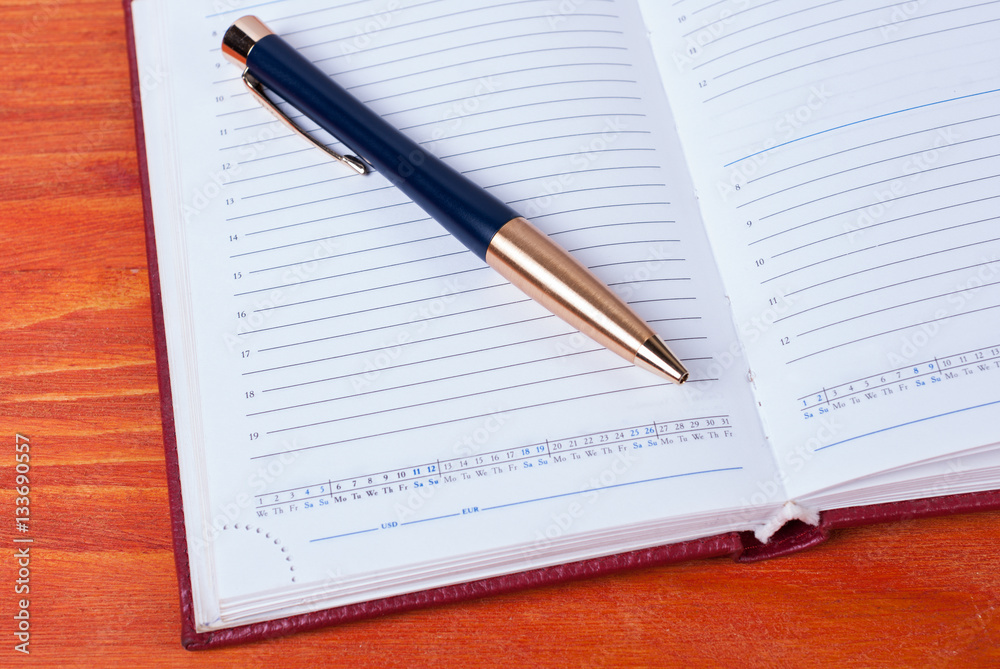 Business accessories - diary with a pen lying on a wooden table Business accessories - diary with a pen lying on a wooden table