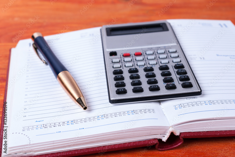 Open notebook with a calculator and a pen lying on it Open notebook with a calculator and a pen lying on it