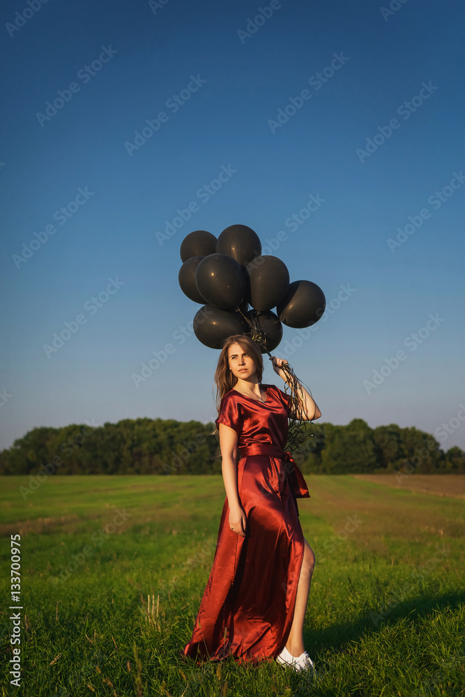 girl in red dress with black balloons standing in a field girl in red dress with black balloons standing in a field