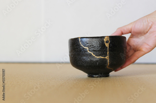 金継された抹茶茶碗を右手で出す畳の和室ぼかした背景