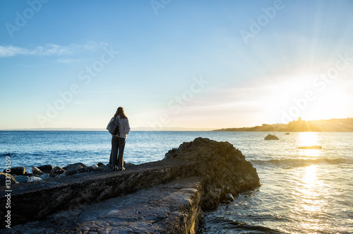 Woman standing close the sea and looking to sunset