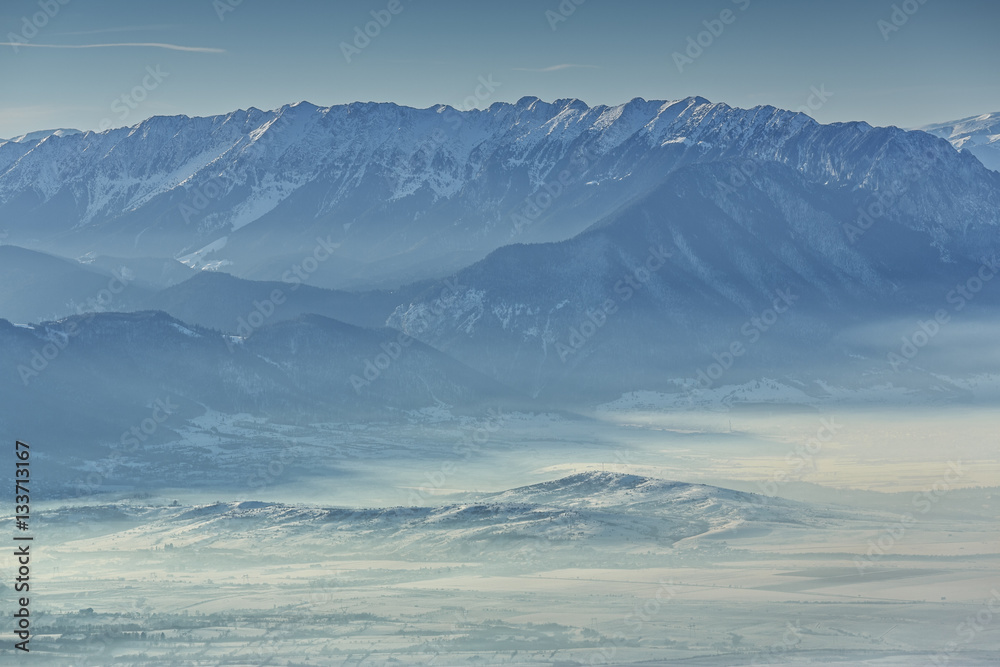 Idyllic winter landscape with snowy Piatra Craiului mountain range and misty valleys in the morning, Romania.