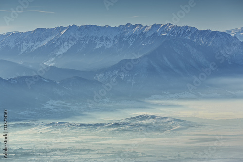 Idyllic winter landscape with snowy Piatra Craiului mountain range and misty valleys in the morning, Romania. © Photosebia