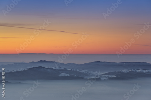 Idyllic winter scenery with sunset over foggy valleys of the Carpathians mountains, Transylvania region, Romania.